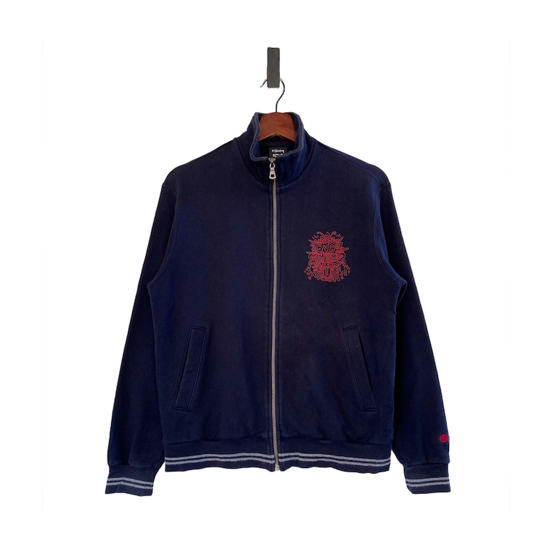 Może przedstawiać: Granatowa bluza zapinana na zamek błyskawiczny z haftowanym czerwonym wzorem z przodu. Wz&oacute;r zawiera słowa "Boys" i "Girls" w stylizowanym wzorze.