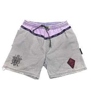 Pode incluir: Calções cinzentos com cós e cordão roxos. Os calções apresentam um design decorativo na perna esquerda e um patch em forma de diamante bordô na perna direita. Os calções têm um aspeto desgastado.