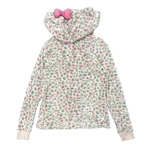 May include: A white hooded sweatshirt with a pink bow on the hood. The sweatshirt has a leopard print pattern in shades of pink, green, and blue.