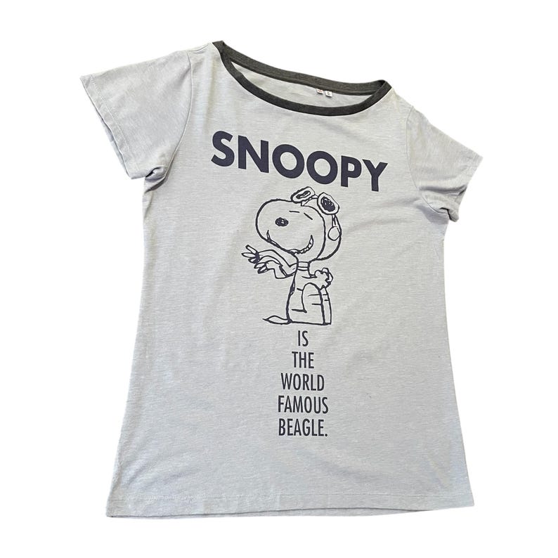 Może przedstawiać: Jasnoszara koszulka z napisem "SNOOPY" w kolorze granatowym nad czarno-białą ilustracją Snoopy'ego w okularach. Poniżej ilustracji znajduje się napis "IS THE WORLD FAMOUS BEAGLE". Koszulka ma ciemnoszary dekolt i kr&oacute;tkie rękawy.