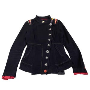 May include: Black jacket with a high collar and silver buttons. The jacket has red lining at the cuffs and decorative shoulder accents. It has a fitted shape and a flared hem. The jacket's design is unique.