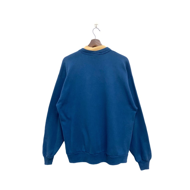May include: A blue sweatshirt with a tan collar. The sweatshirt is hanging on a wooden hanger.