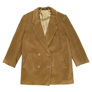 May include: A tan double-breasted blazer with a notched collar and two rows of buttons. The blazer has two front pockets and a light-colored lining. The sleeves are long, and the garment is laid flat on a white background.