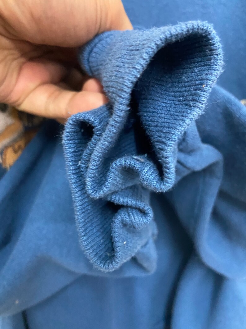 May include: Close-up of the inside of a blue sweatshirt cuff. The fabric is soft and textured.