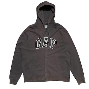 Könnte beinhalten: Ein dunkelgrauer Kapuzenpullover mit einem großen weißen "GAP"-Logo auf der Vorderseite.