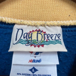 May include: A blue and yellow tag with the text "Day Breeze" and a sun graphic. Below the tag is a white tag with the text "NuBlend" and a size "L" tag. The tag also says "50% Cotton / 50% Polyester Made in U.S.A."