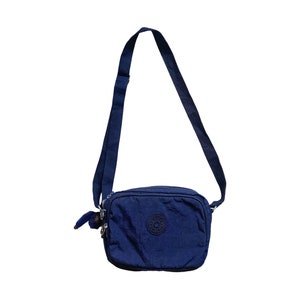 May include: A dark blue crossbody bag with a zipper closure and a small logo on the front.