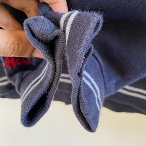 Może przedstawiać: Zbliżenie na prążkowane, granatowe mankiety bluzy z białymi paskami. Mankiet jest podwinięty, odsłaniając wewnętrzną stronę materiału.