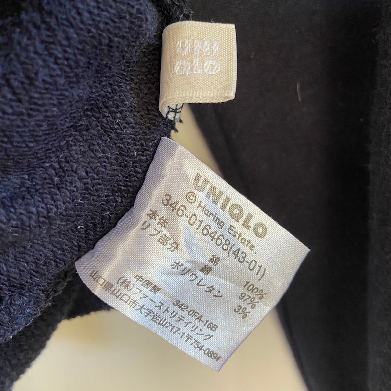 Może przedstawiać: Biała metka z czarnym tekstem, kt&oacute;ry brzmi "UNIQLO Haring Estate. 346-016468(43-01)" i podaje skład tkaniny jako 100% bawełna i 3% poliuretan.