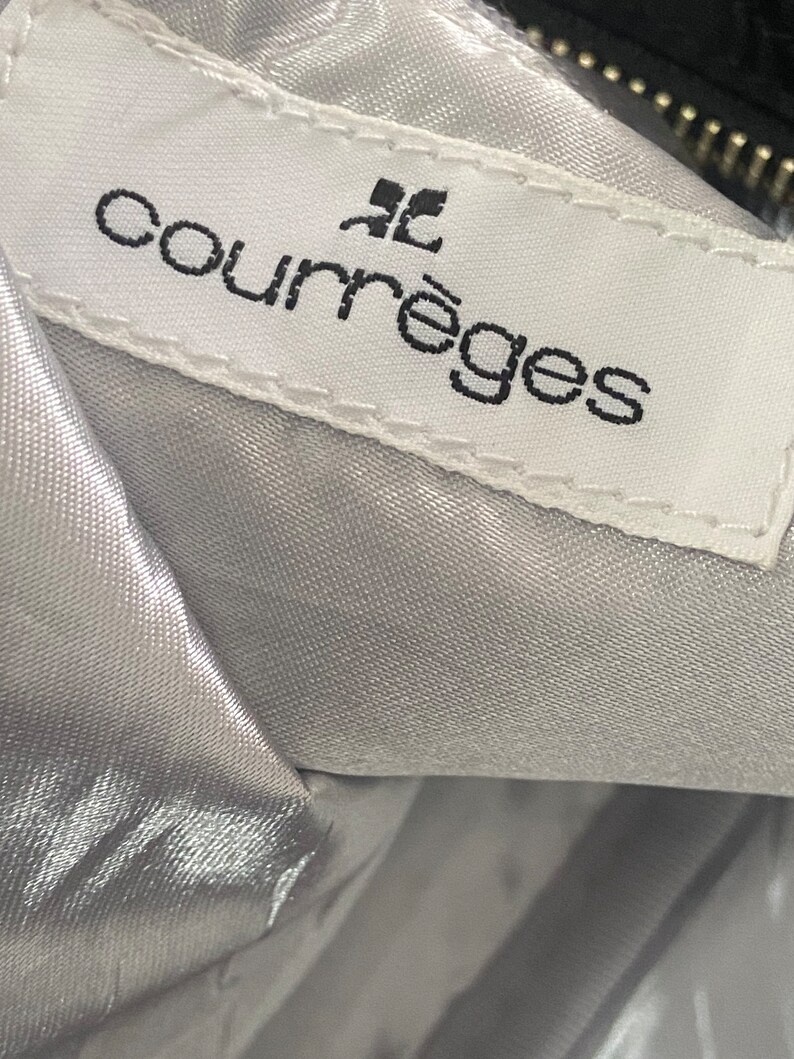 May include: A white label with black text that reads "Courr&egrave;ges" with a small black square above the word "Courr&egrave;ges".