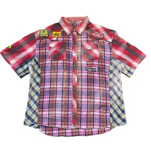 Peut inclure: Une chemise boutonnée à manches courtes avec un motif patchwork. La chemise présente un mélange de motifs à carreaux rouges, roses et bleus, avec des écussons indiquant "Field Masters" et "American Gamble". La chemise a deux poches de poitrine et un col boutonné.