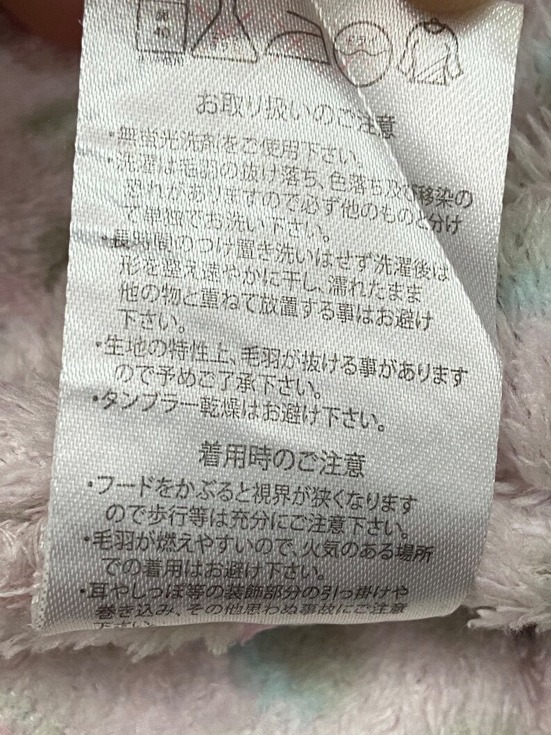 May include: White fabric care label with Japanese text, including instructions for washing, drying, and wearing a hooded garment. The text reads "Care Instructions" and "Wearing Instructions".