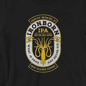 Op de afbeelding: Zwart T-shirt met een gele afbeelding van een bieretiket met een octopus en de tekst "Greyjoy Brewing Co. Ironborn IPA We Do Not Sow What Is Dead May Never Die Iron Islands Export". Het shirt heeft maat informatie gedrukt in de rechter benedenhoek.