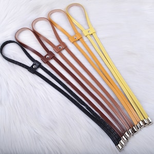 Könnte beinhalten: Fünf Lederriemen in verschiedenen Farben, darunter Schwarz, Braun und Gelb, sind in einer Reihe angeordnet. Die Riemen sind alle gleich lang und haben an jedem Ende eine Schlaufe. Sie werden wahrscheinlich für eine Tasche oder eine Geldbörse verwendet.