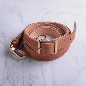 May include: A brown leather strap with a gold metal buckle and hook. The strap is folded and coiled.
