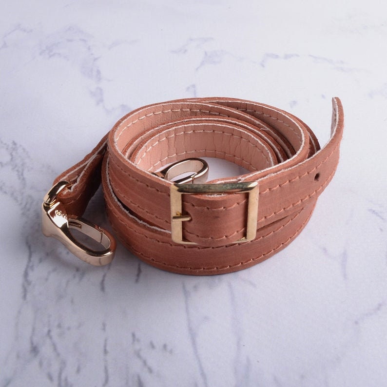 May include: A brown leather strap with a gold metal buckle and hook. The strap is folded and coiled.
