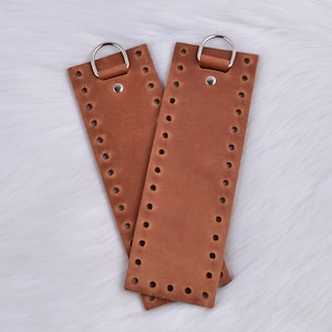 May include: Two brown leather straps with metal rings and holes for stitching. The straps are about 10 inches long and 1 inch wide.