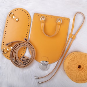 May include: A set of yellow leather crafting supplies for making a small bag. The set includes a bag base, a strap, a handle, and a metal clasp. There is also a spool of yellow yarn.