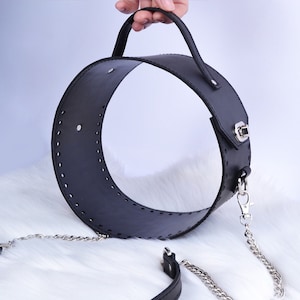 May include: A black leather circle bag with a top handle and a silver chain strap. The bag has a stitched design and a silver clasp.