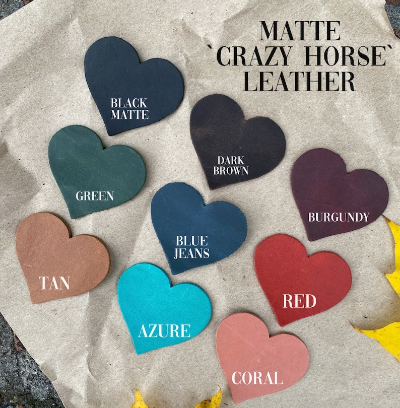 May include: Nine heart-shaped leather swatches in various colors, including black, green, tan, blue, azure, coral, red, burgundy, and dark brown. The swatches are arranged in a circle on a brown paper background. The text "MATTE 'CRAZY HORSE' LEATHER" is written in black at the top of the image.