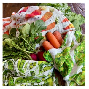May include: Fresh produce, including carrots, radishes, and leafy greens, are nestled in reusable, patterned fabric produce bags. The bags feature carrot and pea pod designs, offering an eco-friendly alternative to plastic.