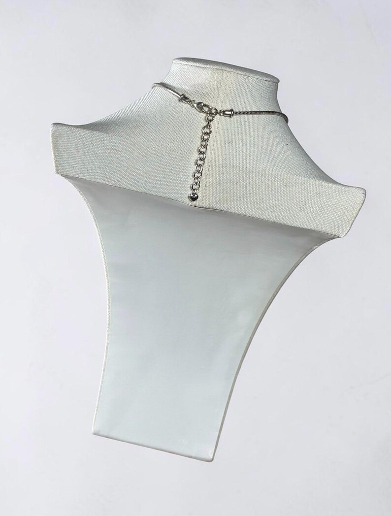 May include: A silver-toned necklace chain featuring a snake chain design and a lobster claw clasp. An adjustable extender chain is attached to the clasp, ending with a small heart-shaped charm. The metal has a polished, reflective finish.