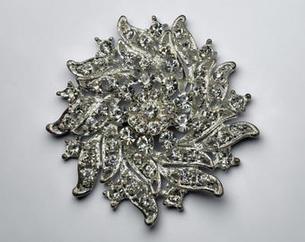 Broche vintage plateado con diseño floral en forma de explosión, adornado con diamantes de imitación transparentes.