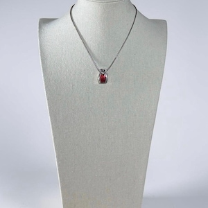 May include: A silver-toned necklace featuring a small, rectangular pendant with a vibrant red center inlay. The pendant is suspended from a thin, delicate silver-toned chain, creating a simple and refined piece of jewelry for everyday wear.