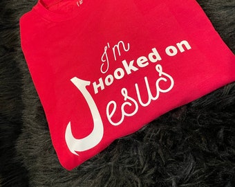 May include: Red t-shirt with a white hook and the text "I'm Hooked on Jesus".