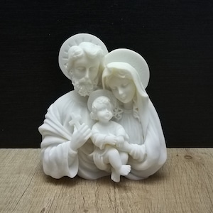 Puede incluir: Escultura de cer&aacute;mica blanca de la Sagrada Familia. La escultura representa a Mar&iacute;a, Jos&eacute; y el ni&ntilde;o Jes&uacute;s. Las figuras est&aacute;n de pie, juntas, con Mar&iacute;a sosteniendo a Jes&uacute;s en sus brazos. Jos&eacute; est&aacute; de pie detr&aacute;s de Mar&iacute;a, con su mano sobre su hombro. La escultura es una representaci&oacute;n tradicional de la Sagrada Familia.