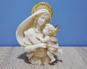 May include: A white ceramic statue of the Virgin Mary holding a baby Jesus. The statue has gold accents on the halo and the baby's wings.