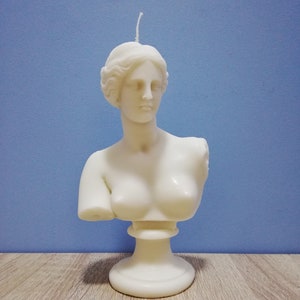 Peut inclure: Bougie blanche en forme de buste féminin classique. La bougie représente la tête, les épaules et le haut du torse en détail, avec une mèche en haut. Le buste est monté sur un socle. La bougie est en cire.
