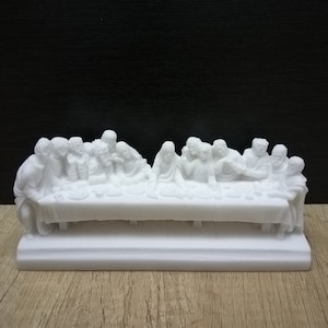 May include: White marble sculpture depicting the Last Supper. The sculpture shows Jesus and his disciples seated around a table, with Jesus in the center. The sculpture is detailed and realistic, with each figure having distinct features.