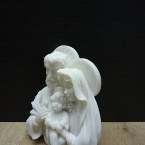 Puede incluir: Escultura de cer&aacute;mica blanca de la Sagrada Familia. La escultura representa a Mar&iacute;a, Jos&eacute; y el ni&ntilde;o Jes&uacute;s. Mar&iacute;a sostiene a Jes&uacute;s en sus brazos y Jos&eacute; est&aacute; de pie detr&aacute;s de ellos con el brazo alrededor del hombro de Mar&iacute;a.