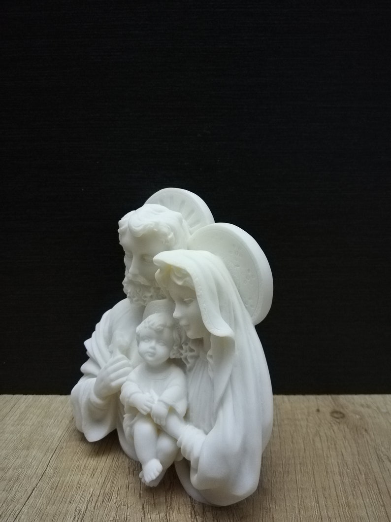 Puede incluir: Escultura de cer&aacute;mica blanca de la Sagrada Familia. La escultura representa a Mar&iacute;a, Jos&eacute; y el ni&ntilde;o Jes&uacute;s. Mar&iacute;a sostiene a Jes&uacute;s en sus brazos y Jos&eacute; est&aacute; de pie detr&aacute;s de ellos con el brazo alrededor del hombro de Mar&iacute;a.