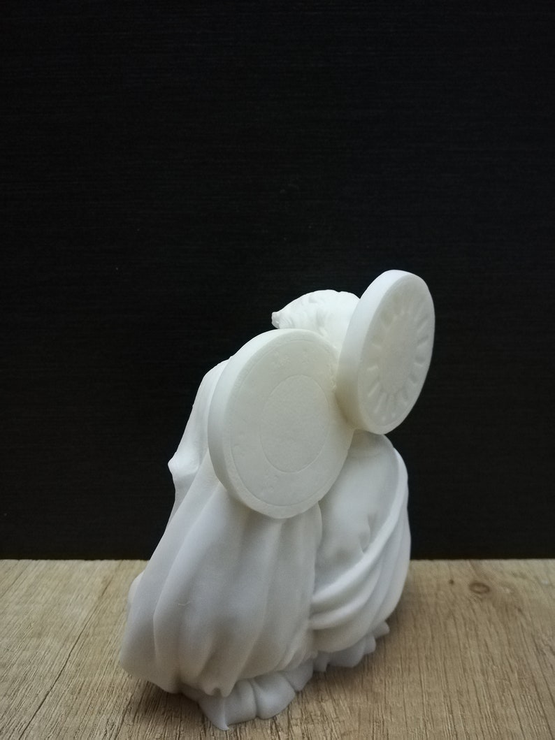 Puede incluir: Escultura de cer&aacute;mica blanca de una persona que lleva una capa con dos objetos circulares grandes en la cabeza.
