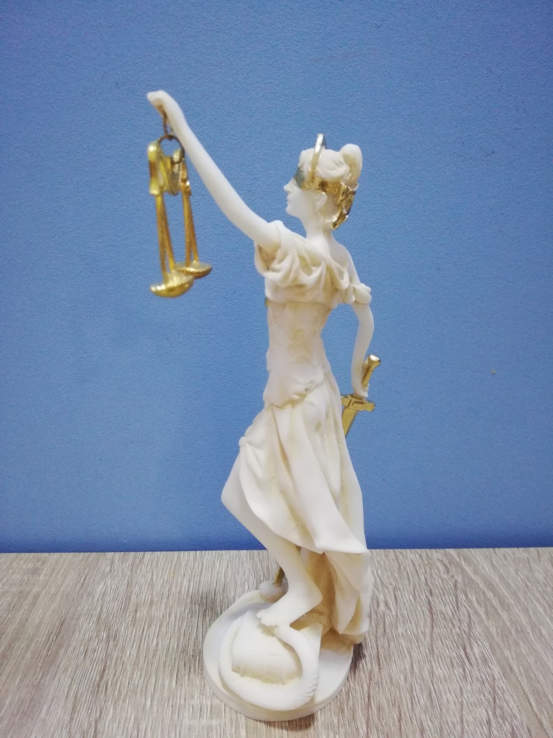 Puede incluir: Estatua de m&aacute;rmol blanco de la diosa griega de la justicia, Temis, sosteniendo una espada y una balanza. La estatua est&aacute; de pie sobre una base redonda.