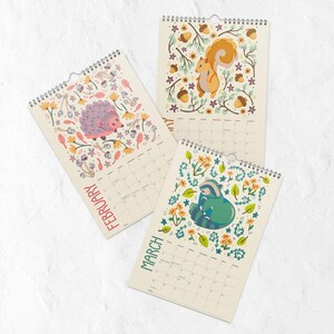 A 2026 wall calendar featuring colourful folk-art animal illustrations displayed in a flat lay. Wire-bound with premium thick paper, this illustrated monthly calendar showcases vibrant artwork for each month. Ideal for shoppers looking for a 2026 calendar, animal art calendar, home décor calendar, or unique artist-designed wall calendar.