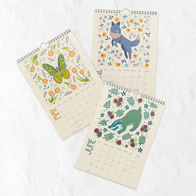A 2026 wall calendar featuring colourful folk-art animal illustrations displayed in a flat lay. Wire-bound with premium thick paper, this illustrated monthly calendar showcases vibrant artwork for each month. Ideal for shoppers looking for a 2026 calendar, animal art calendar, home décor calendar, or unique artist-designed wall calendar.