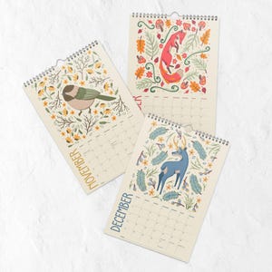 A 2026 wall calendar featuring colourful folk-art animal illustrations displayed in a flat lay. Wire-bound with premium thick paper, this illustrated monthly calendar showcases vibrant artwork for each month. Ideal for shoppers looking for a 2026 calendar, animal art calendar, home décor calendar, or unique artist-designed wall calendar.