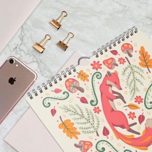 A 2026 wall calendar featuring colourful folk-art animal illustrations displayed in a flat lay. Wire-bound with premium thick paper, this illustrated monthly calendar showcases vibrant artwork for each month. Ideal for shoppers looking for a 2026 calendar, animal art calendar, home décor calendar, or unique artist-designed wall calendar.