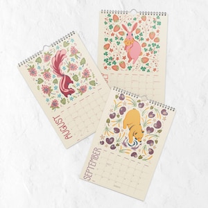 A 2026 wall calendar featuring colourful folk-art animal illustrations displayed in a flat lay. Wire-bound with premium thick paper, this illustrated monthly calendar showcases vibrant artwork for each month. Ideal for shoppers looking for a 2026 calendar, animal art calendar, home décor calendar, or unique artist-designed wall calendar.