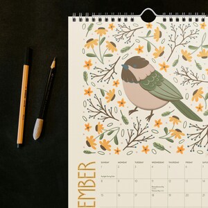 Close-up view of a 2026 wall calendar page showing a detailed folk-art animal illustration printed on thick 271 g/m² paper. Features a wire-bound top and clean monthly layout. Perfect for buyers searching for illustrated calendars, animal-themed art, colourful 2026 wall calendars, or decorative monthly hanging calendars