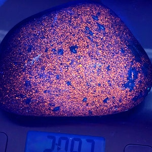 Puede incluir: Una roca redondeada y moteada con un vibrante patrón naranja y azul. La roca está sobre una báscula digital, que muestra un peso de 94,4 kg.