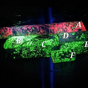 May include: A collection of fluorescent minerals, each with unique patterns and colors. The top piece glows red and green, while the others exhibit vibrant green hues. The minerals are arranged against a dark background.