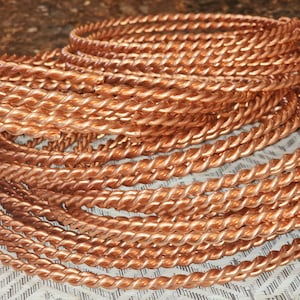 May include: A collection of copper-colored, twisted metal hoops. The hoops are stacked and coiled, showcasing a textured, rope-like design. The warm, metallic hue suggests a craft or jewelry-making theme.