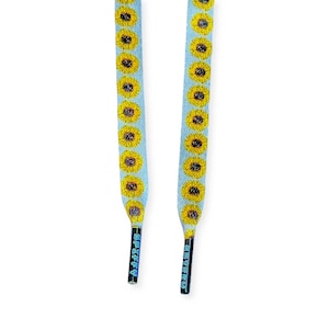 May include: Two light blue shoelaces with a repeating pattern of yellow sunflowers. The shoelaces have black and silver tips with the word "SPIFFY" printed on them.