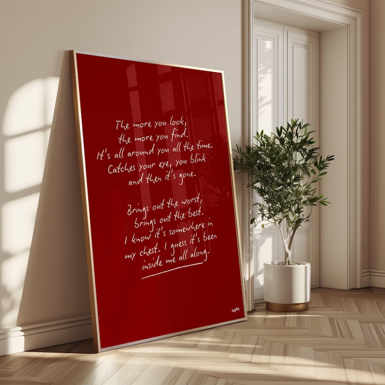 K&ouml;nnte beinhalten: Gerahmter roter Kunstdruck mit goldenem Rahmen, der an einer Wand lehnt. Der Druck zeigt handgeschriebenen wei&szlig;en Text, ein Gedicht oder ein Zitat. Rechts vom Druck ist eine Topfpflanze zu sehen.