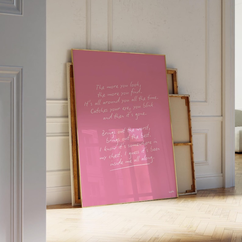 K&ouml;nnte beinhalten: Ein gerahmter rosa Kunstdruck mit goldenem Rahmen, der an einer Wand lehnt. Der Druck zeigt handgeschriebenen wei&szlig;en Text, ein Gedicht &uuml;ber Gef&uuml;hle. Das Kunstwerk befindet sich in einem hellen Raum.