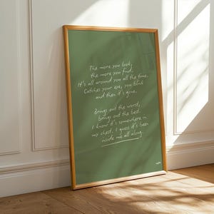 K&ouml;nnte beinhalten: Ein gerahmter Druck mit gr&uuml;nem Hintergrund und goldenem Rahmen. Der Druck zeigt handgeschriebenen wei&szlig;en Text mit einem Gedicht &uuml;ber das Finden von etwas, das schon immer da war. Der Rahmen lehnt an einer wei&szlig;en Wand und einem Holzboden.